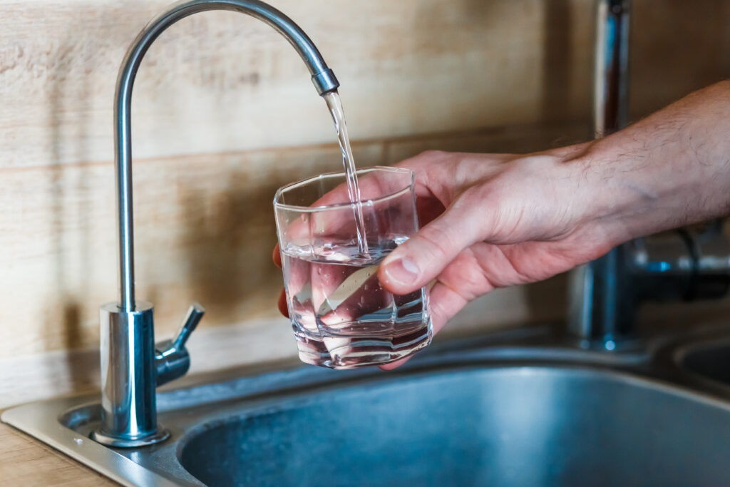 A hand holds a glass under a kitchen faucet as water pours into it.