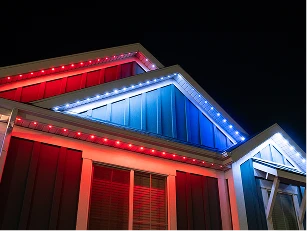 The exterior of a house at night is lit with red, white, and blue lights along the roofline.