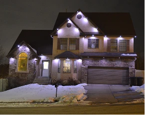 Two-story house with stone accents and a double garage, illuminated by exterior lights at night with patches of snow on the ground.