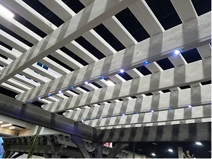 Wooden pergola structure with evenly spaced beams and small built-in LED lights, casting shadows on the area below.