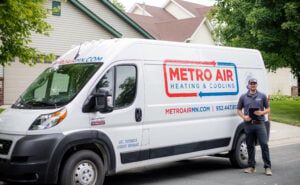 Metro Air Heating & Cooling white service van parked in residential driveway with uniformed technician standing beside it.